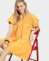 Woman in a yellow dress sitting on a red chair against a white background