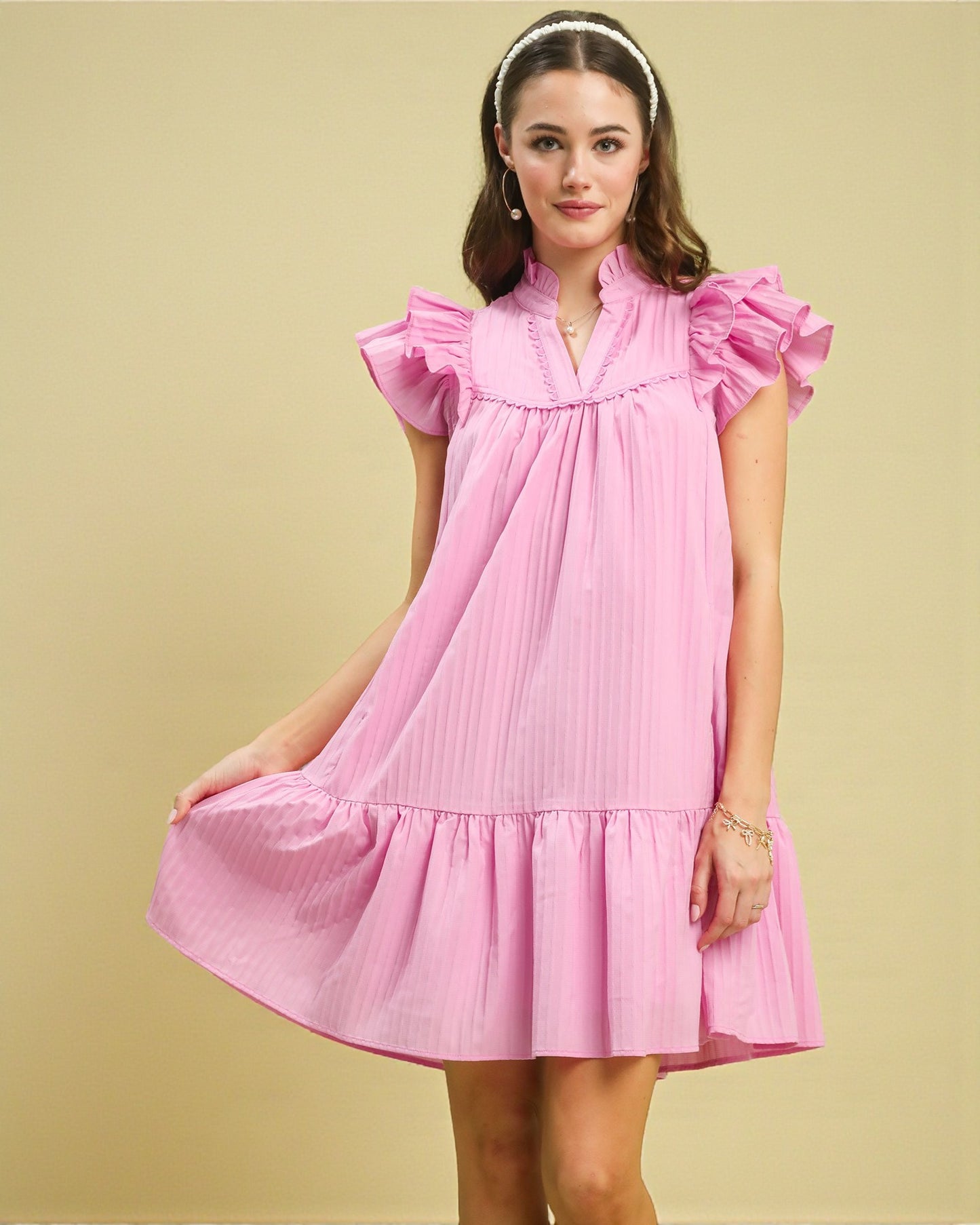 Woman wearing a pink dress with ruffled sleeves on a beige background