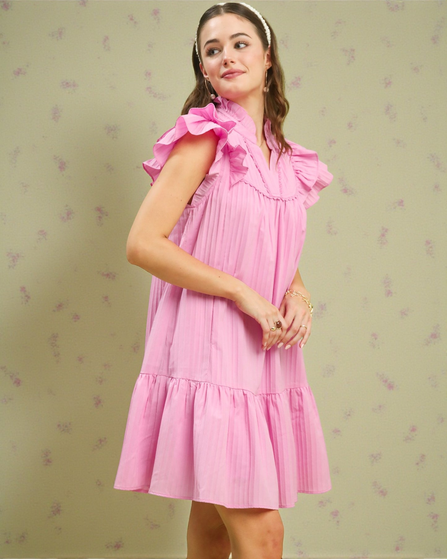 Woman wearing a pink dress with ruffled sleeves on a light green background