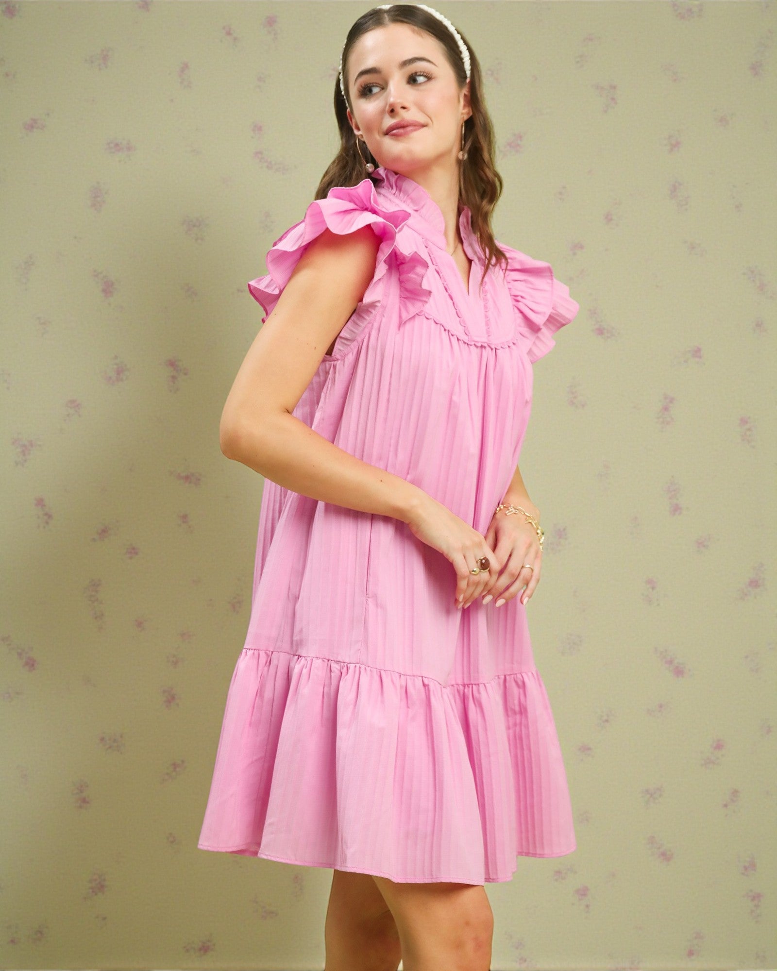 Woman wearing a pink dress with ruffled sleeves on a light green background