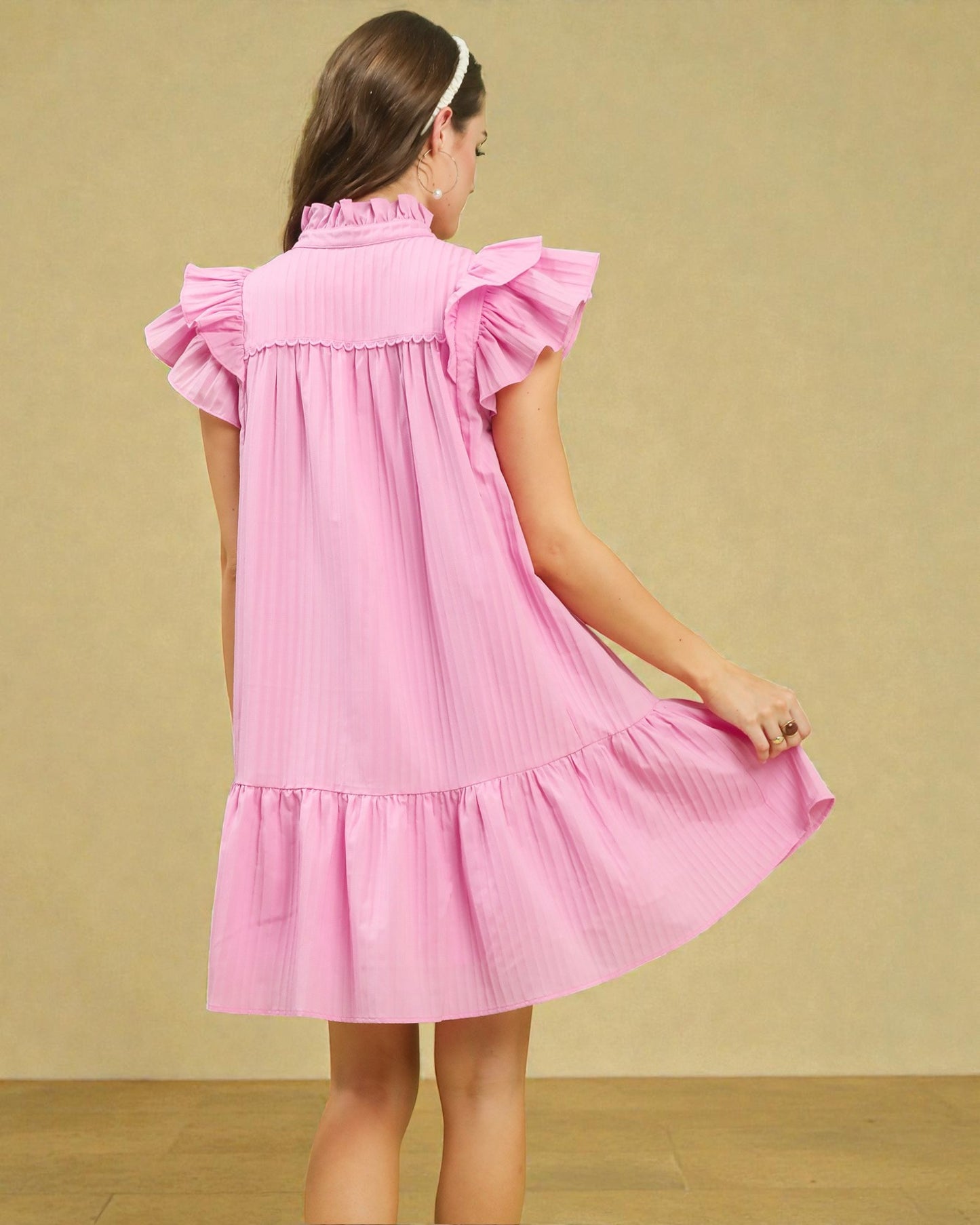 Pink dress with ruffled sleeves and bottom worn by a person on a beige background