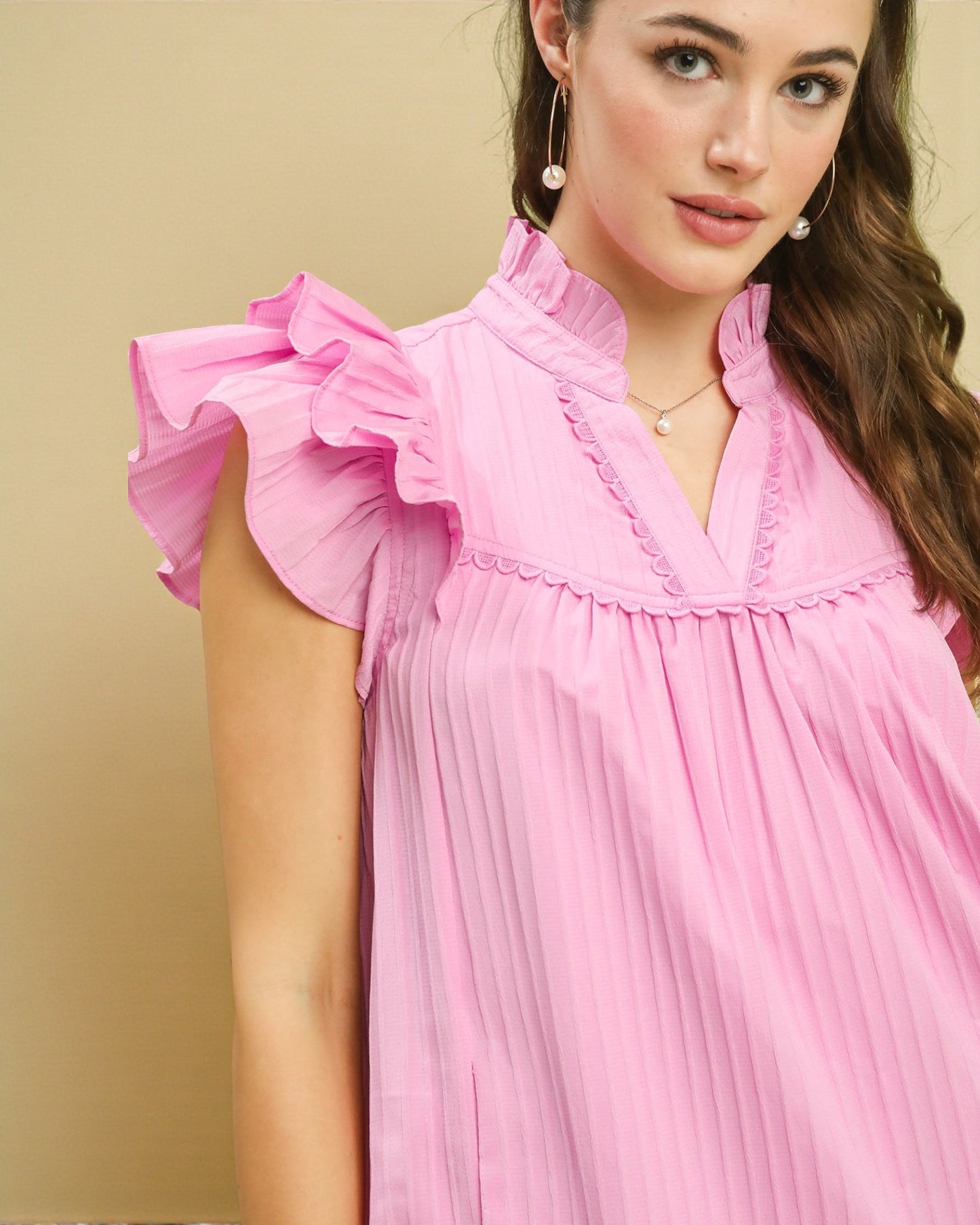 Woman wearing a pink dress with ruffled sleeves against a beige background