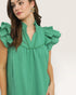 Woman wearing a green dress with ruffled shoulders on a plain background