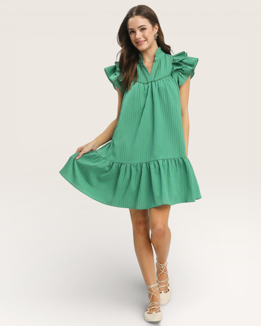 Woman wearing a green dress with ruffled sleeves and hem on a white background