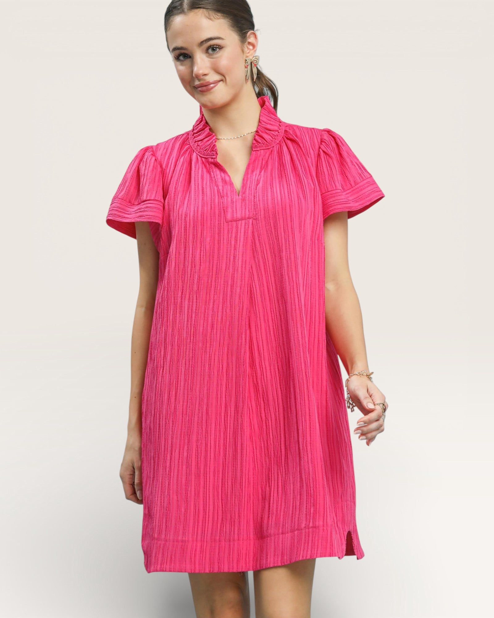 Woman wearing a pink pleated dress against a plain background
