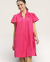 Woman wearing a pink pleated dress against a plain background