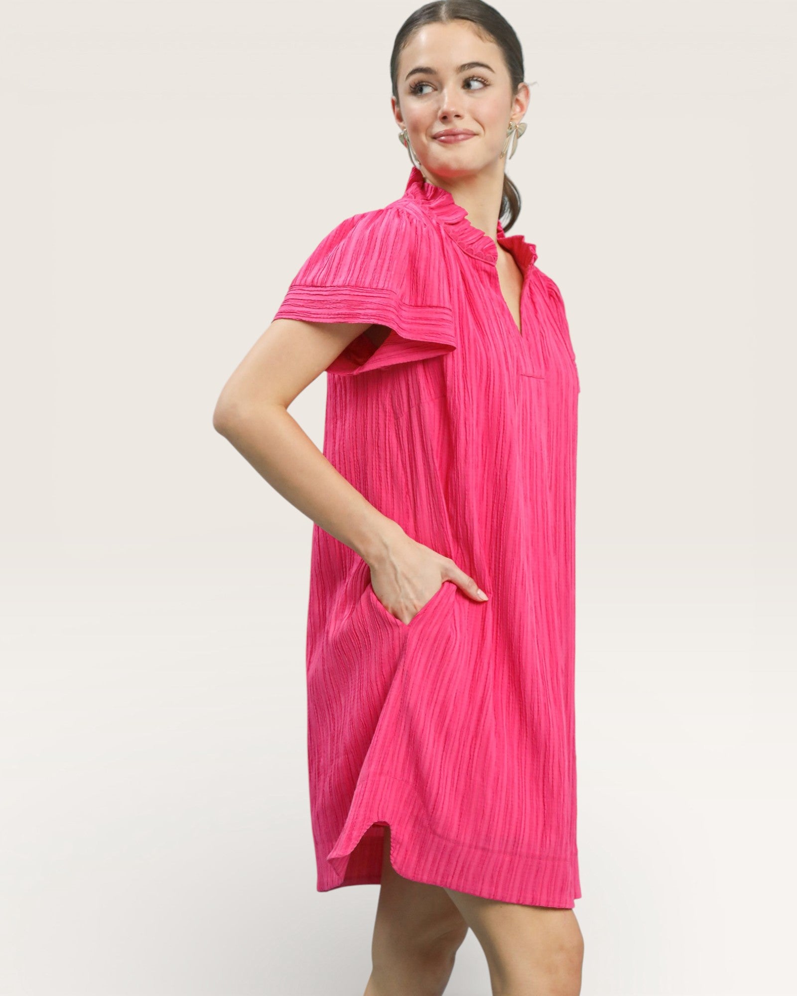 Woman wearing a bright pink pleated dress against a white background