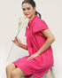 Woman in a pink dress holding a flower against a plain background