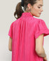 Woman wearing a bright pink pleated dress against a plain background