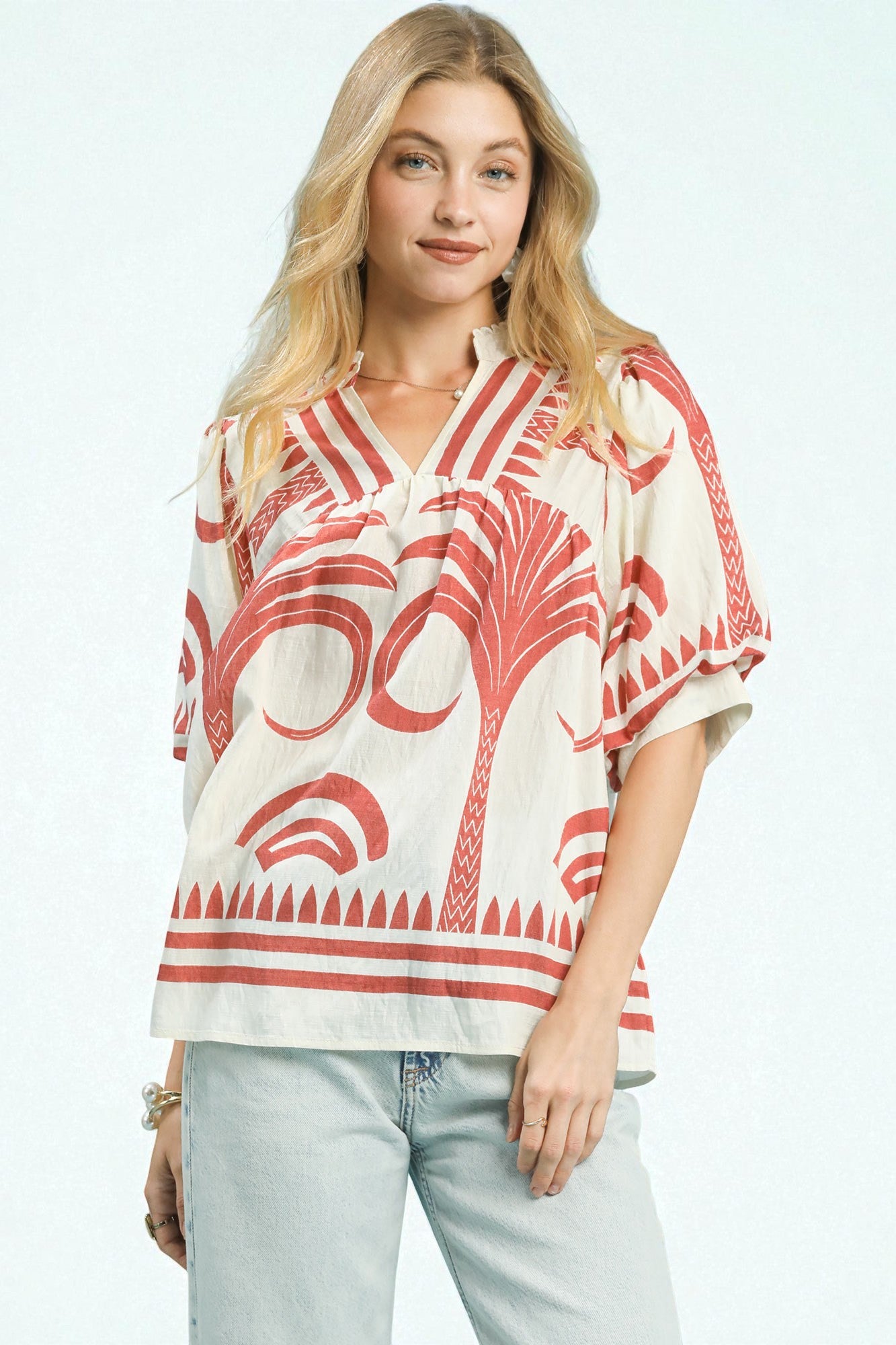 Woman wearing a red and white patterned blouse with light blue jeans on a white background