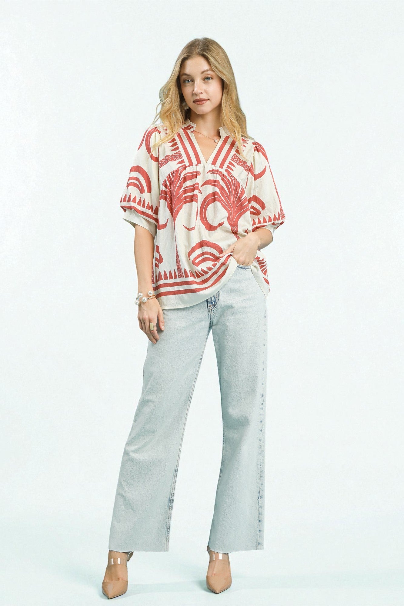 Woman wearing a red and white patterned blouse with light blue jeans on a white background