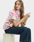 Woman wearing a colorful floral blouse and blue jeans sitting on a white block.