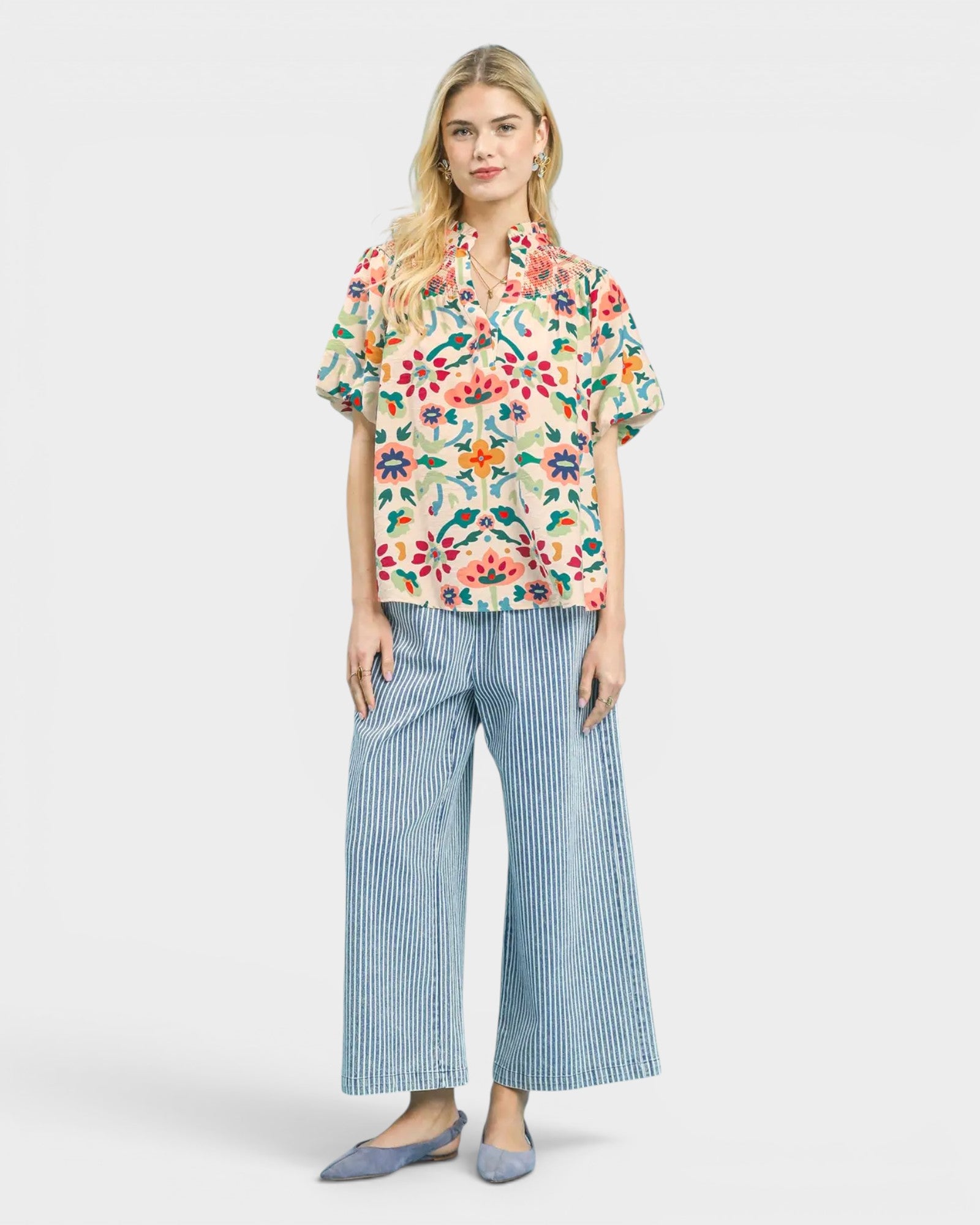 Woman wearing a floral blouse and wide-leg pants on a white background