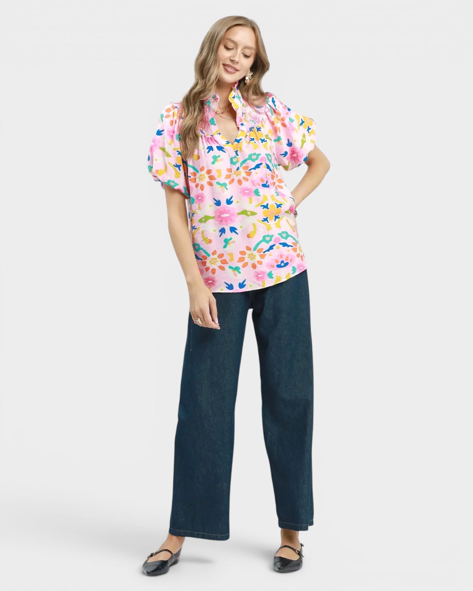 Woman wearing a colorful floral blouse and dark jeans on a white background