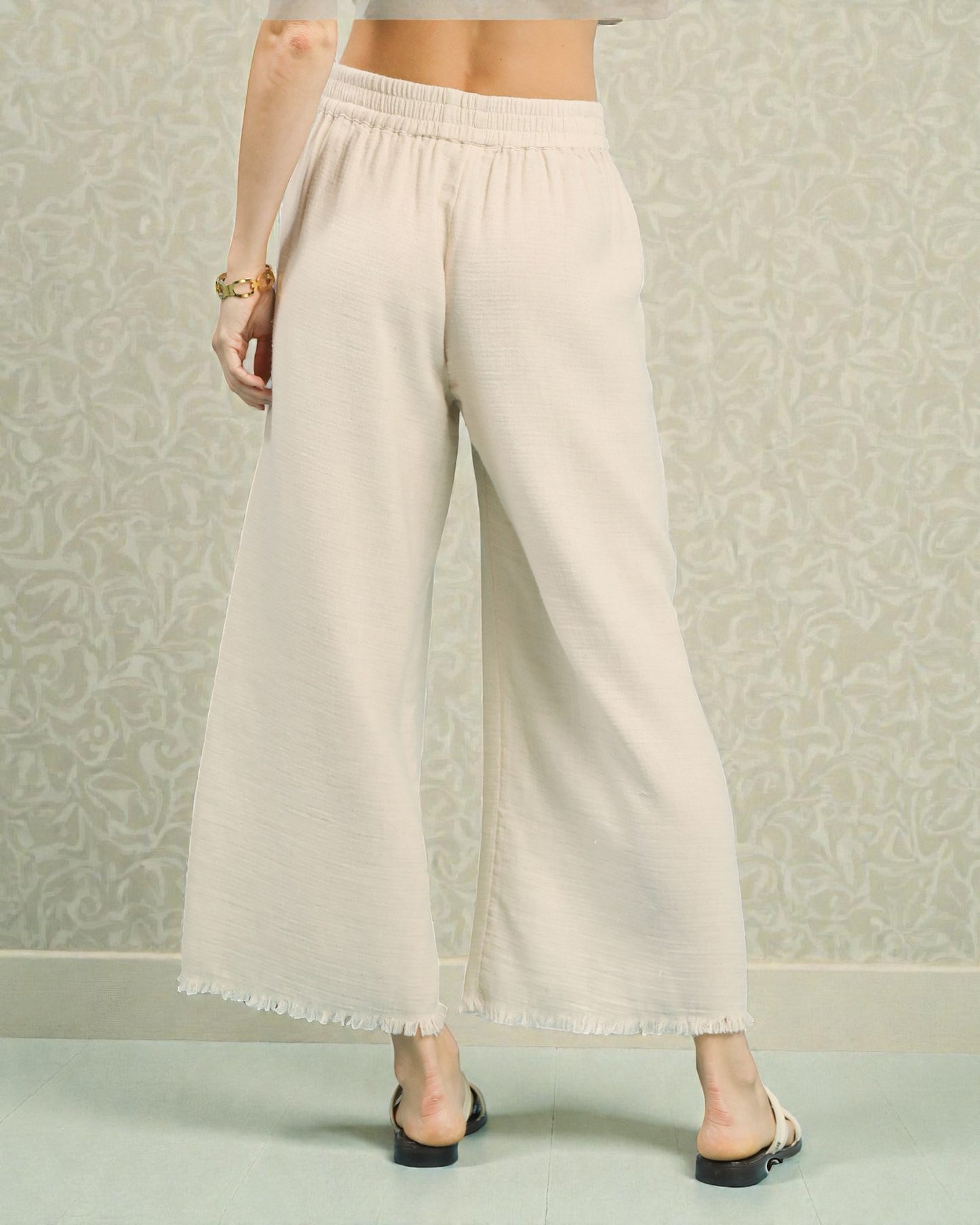 Beige wide-leg pants worn by a person against a light green patterned wall.