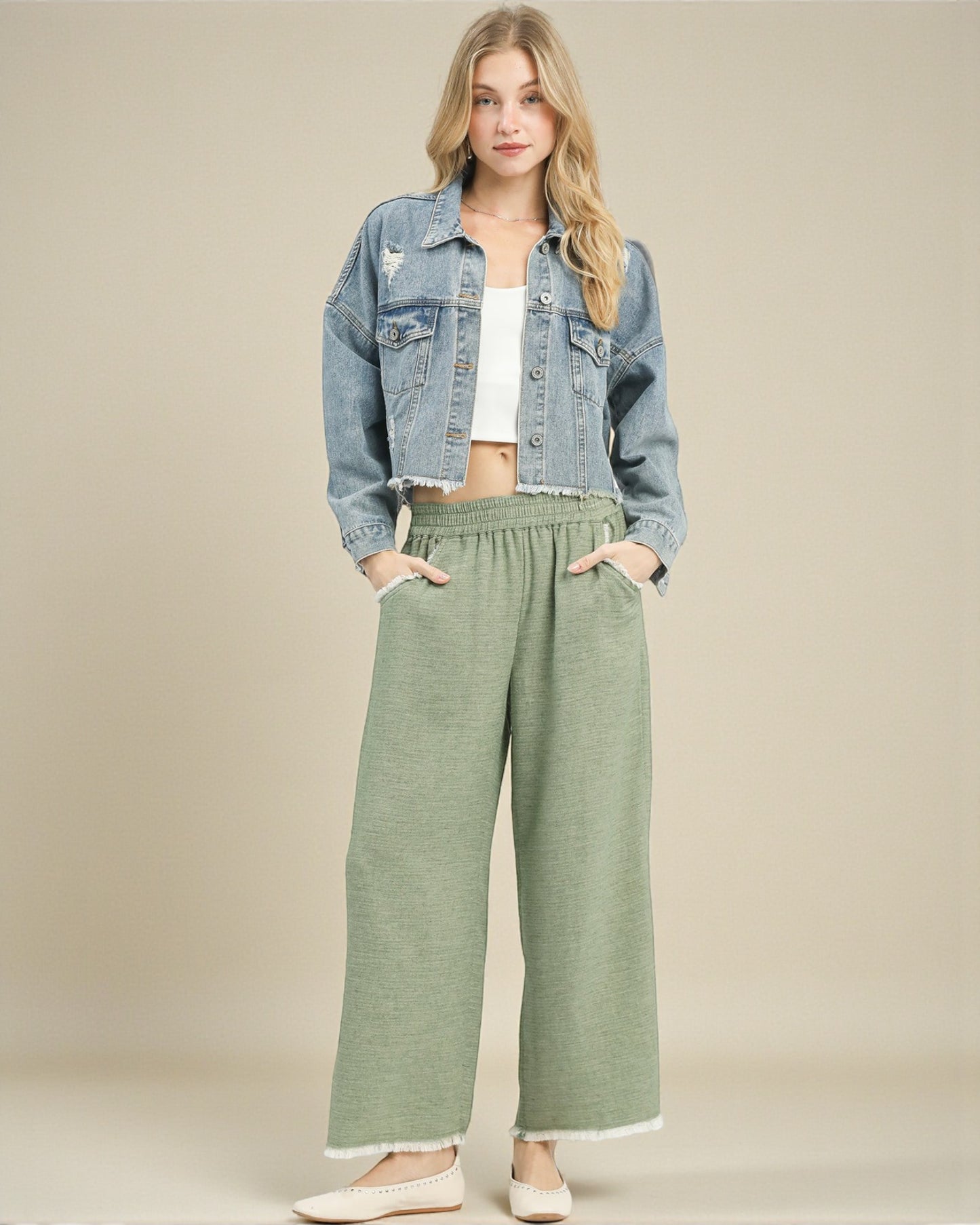 Woman wearing a denim jacket and green pants on a beige background