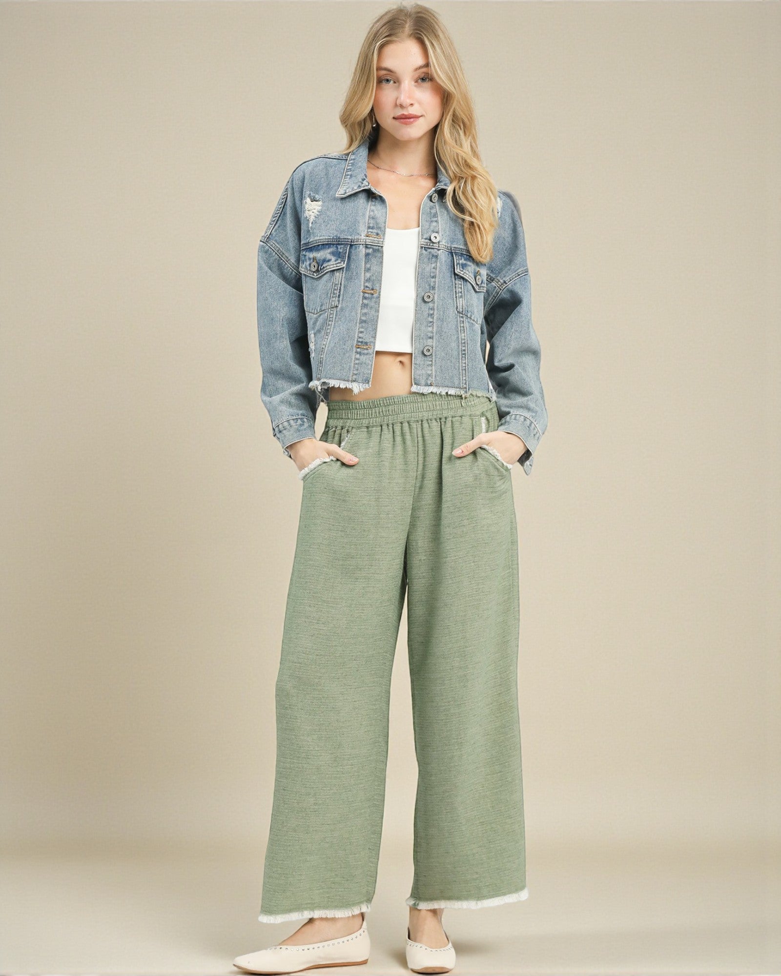 Woman wearing a denim jacket and green pants on a beige background