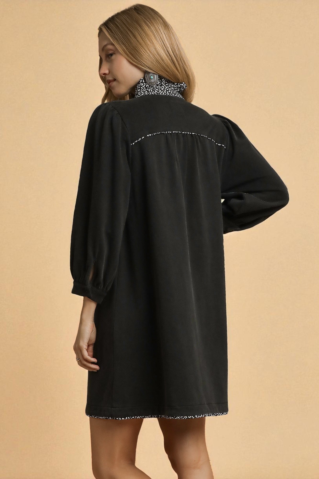 Woman wearing a black dress with intricate detailing on a beige background