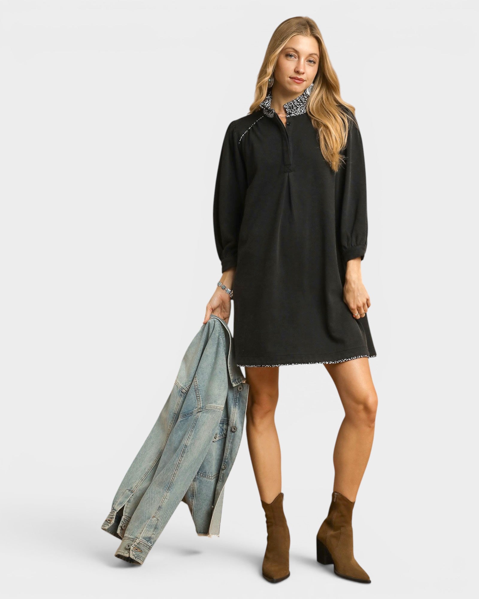 Woman wearing a black dress holding a denim jacket on a white background
