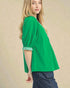 Woman wearing a green blouse with rolled-up sleeves against a beige background