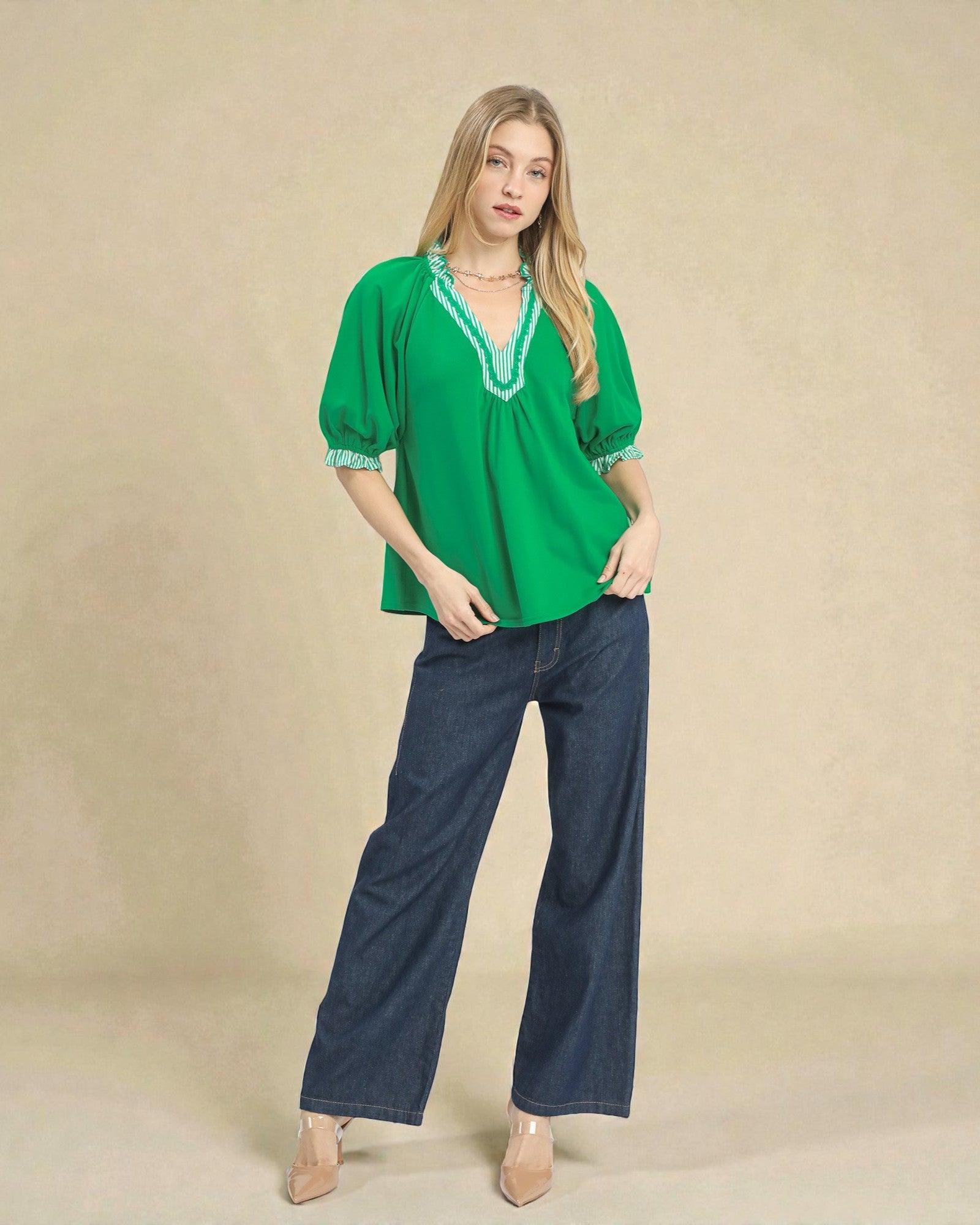 Woman wearing a green blouse and blue pants against a beige background