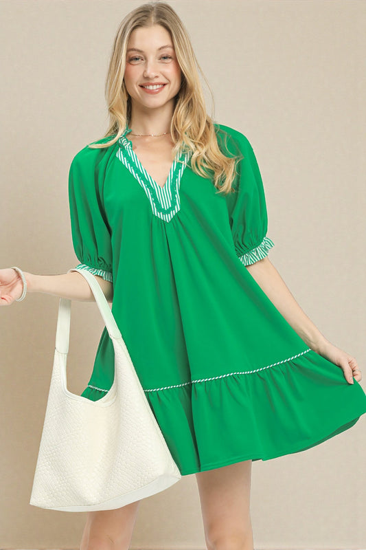 Woman wearing a green dress with white trim holding a white bag against a beige background