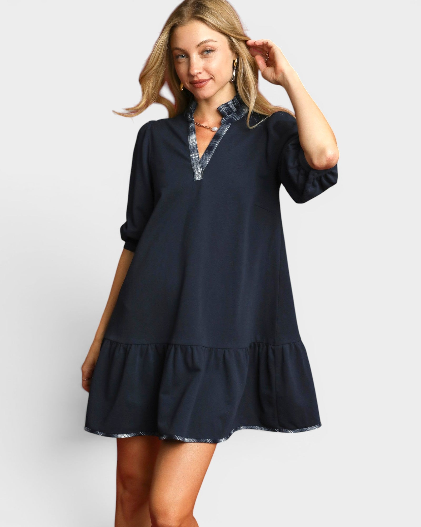 Woman wearing a navy blue dress with plaid trim on a white background