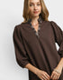 Woman wearing a brown blouse with plaid trim on a white background