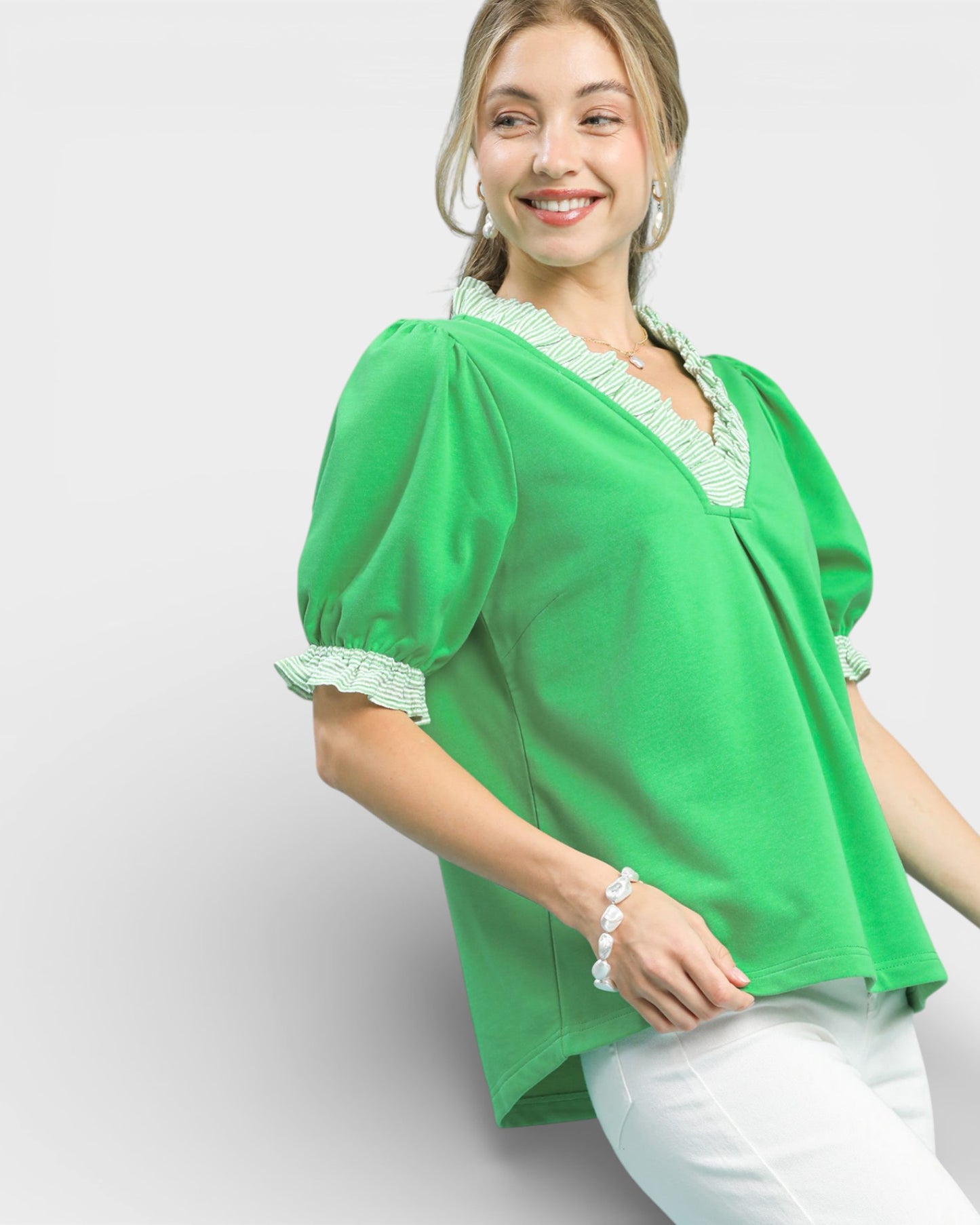 Woman wearing a green blouse with lace details on a light gray background
