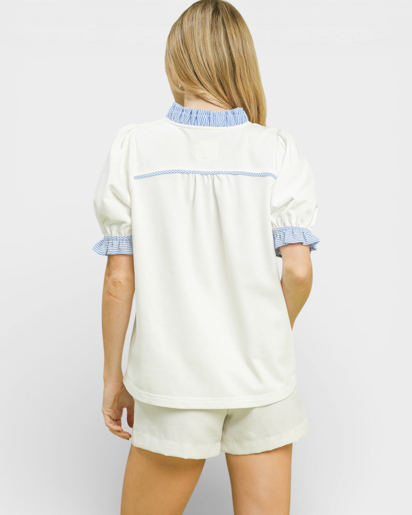 Woman wearing a white pajama set with blue trim on a plain background