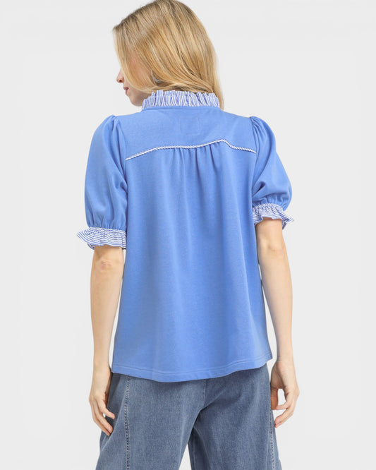 Woman wearing a blue blouse with white trim on a plain background