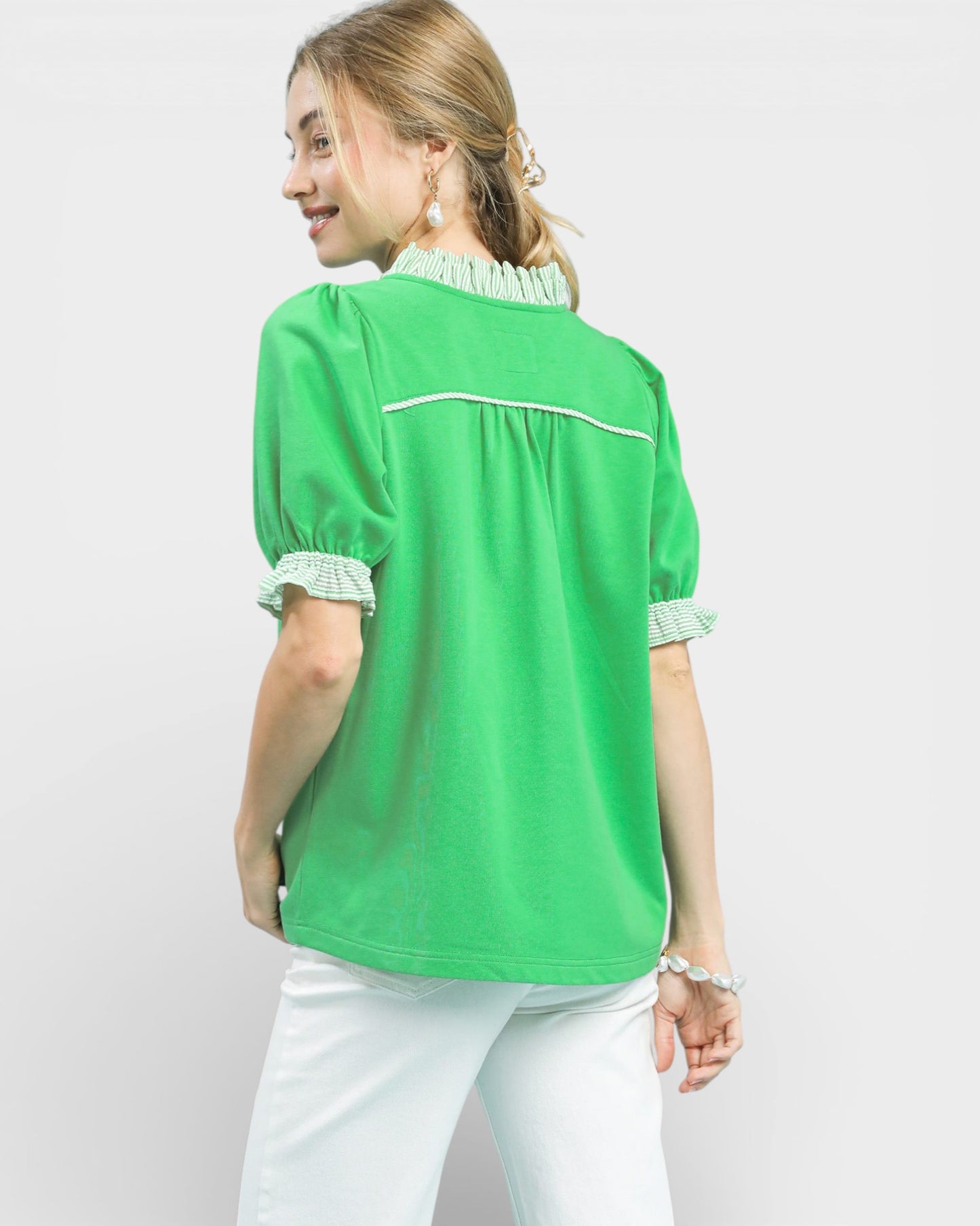 Woman wearing a green blouse with white trim on a plain background