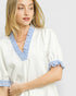 Woman wearing a white blouse with blue trim on a plain background