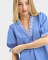 Woman wearing a blue blouse with white trim on a light gray background