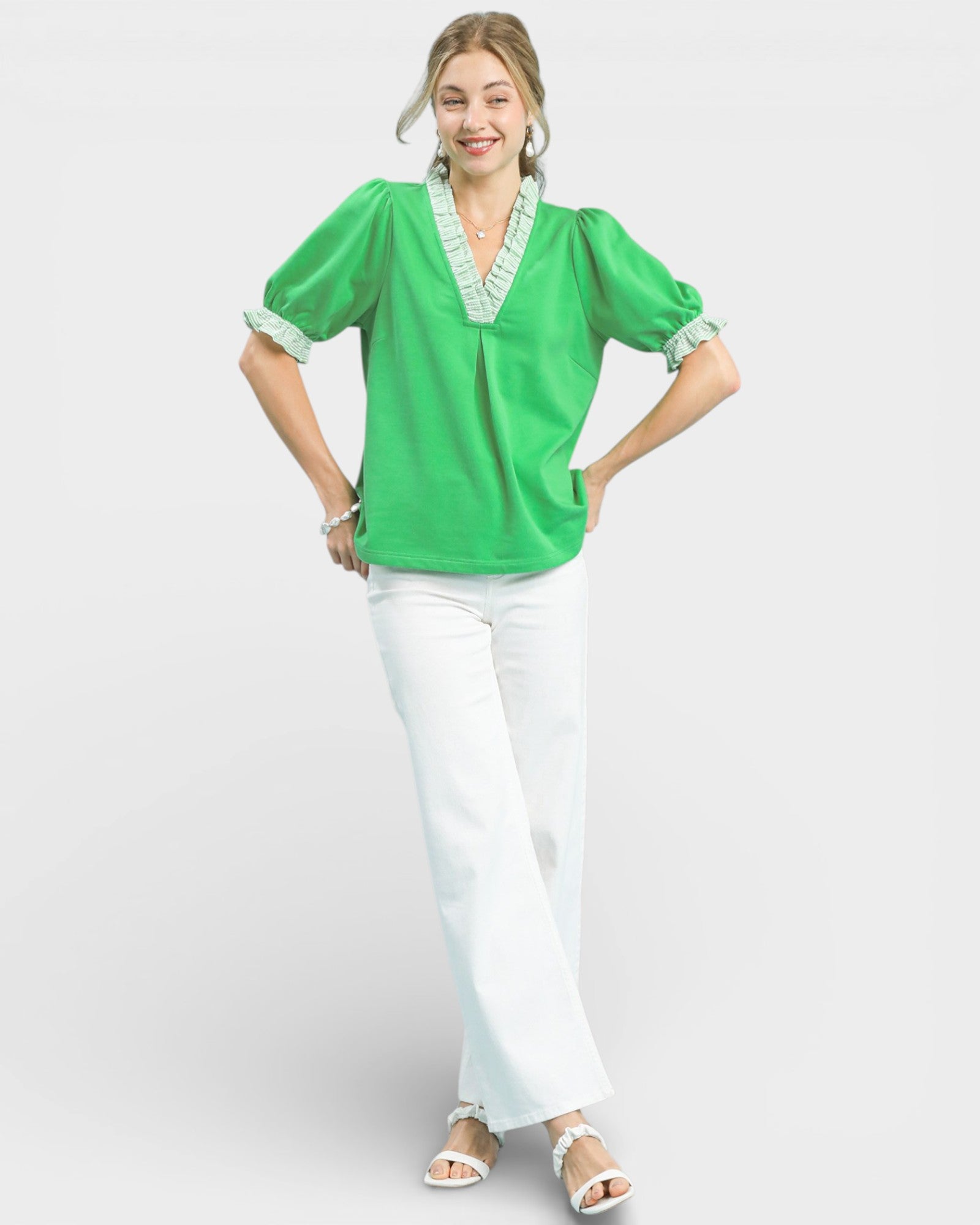 Woman wearing a green blouse with white trim and white pants on a light gray background