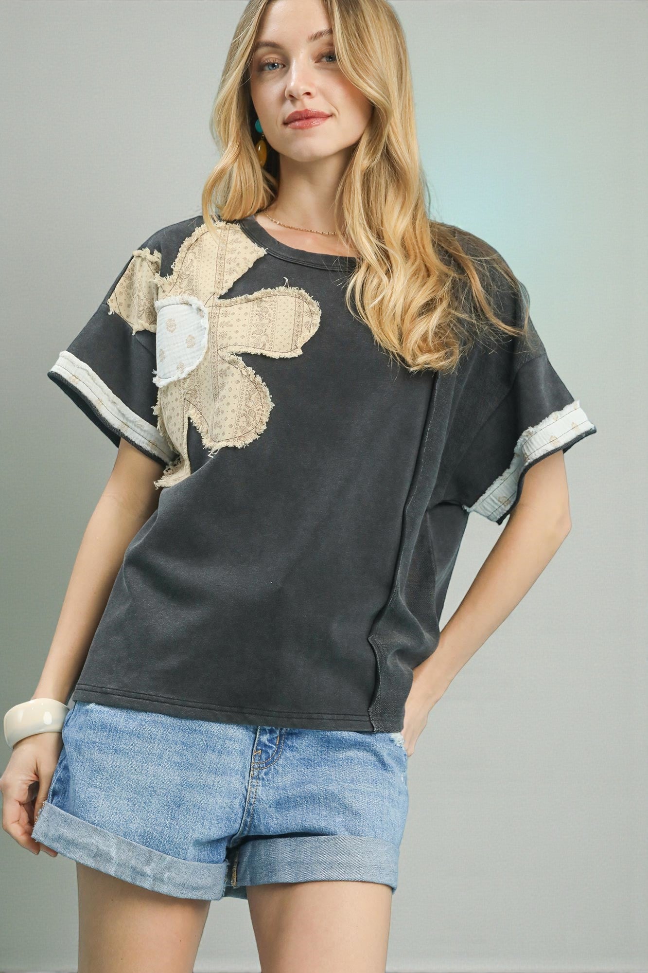 Woman wearing a black t-shirt with a floral design and denim shorts on a gray background