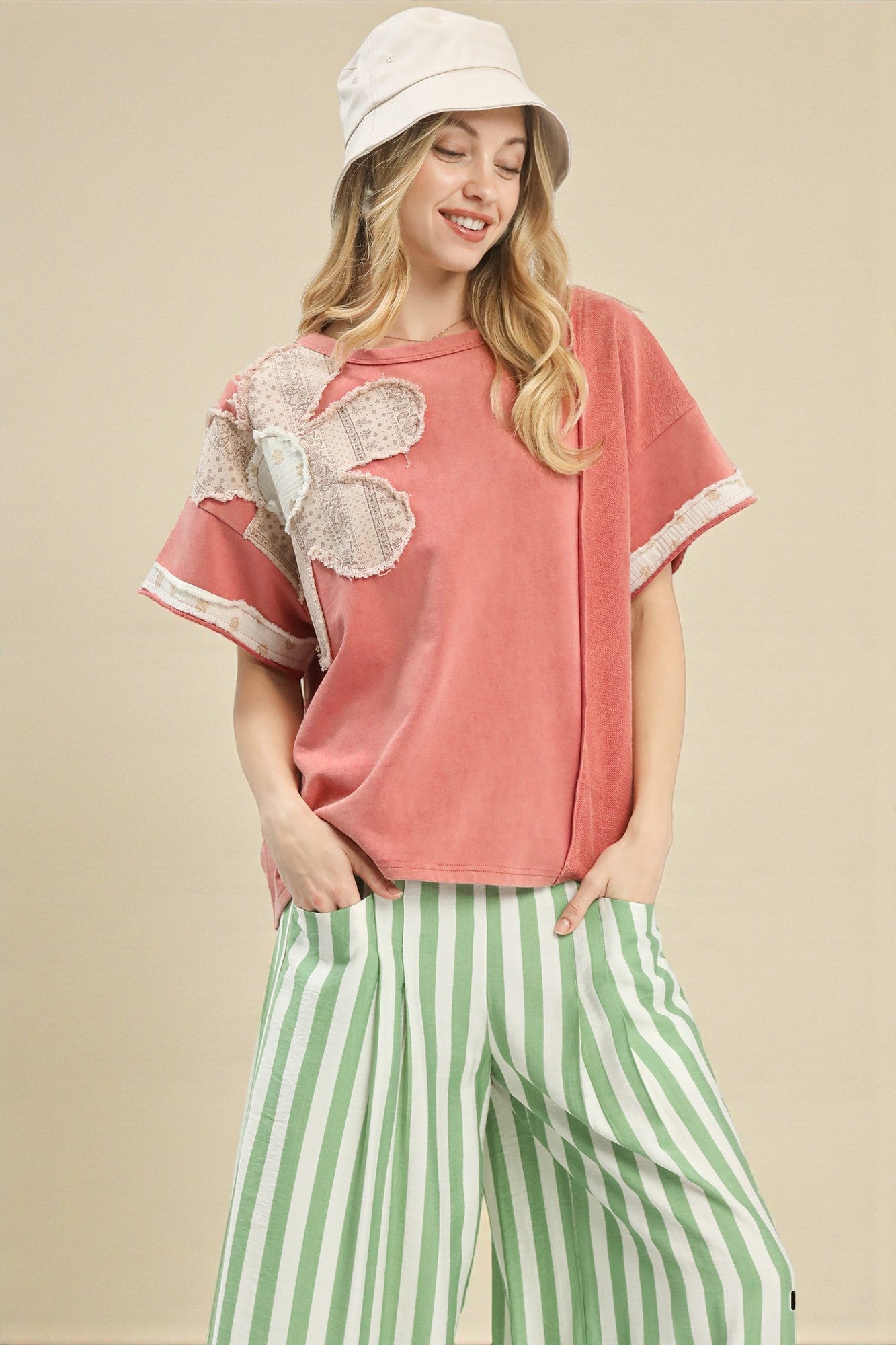 Woman wearing a pink top with floral sleeves and green striped pants on a beige background