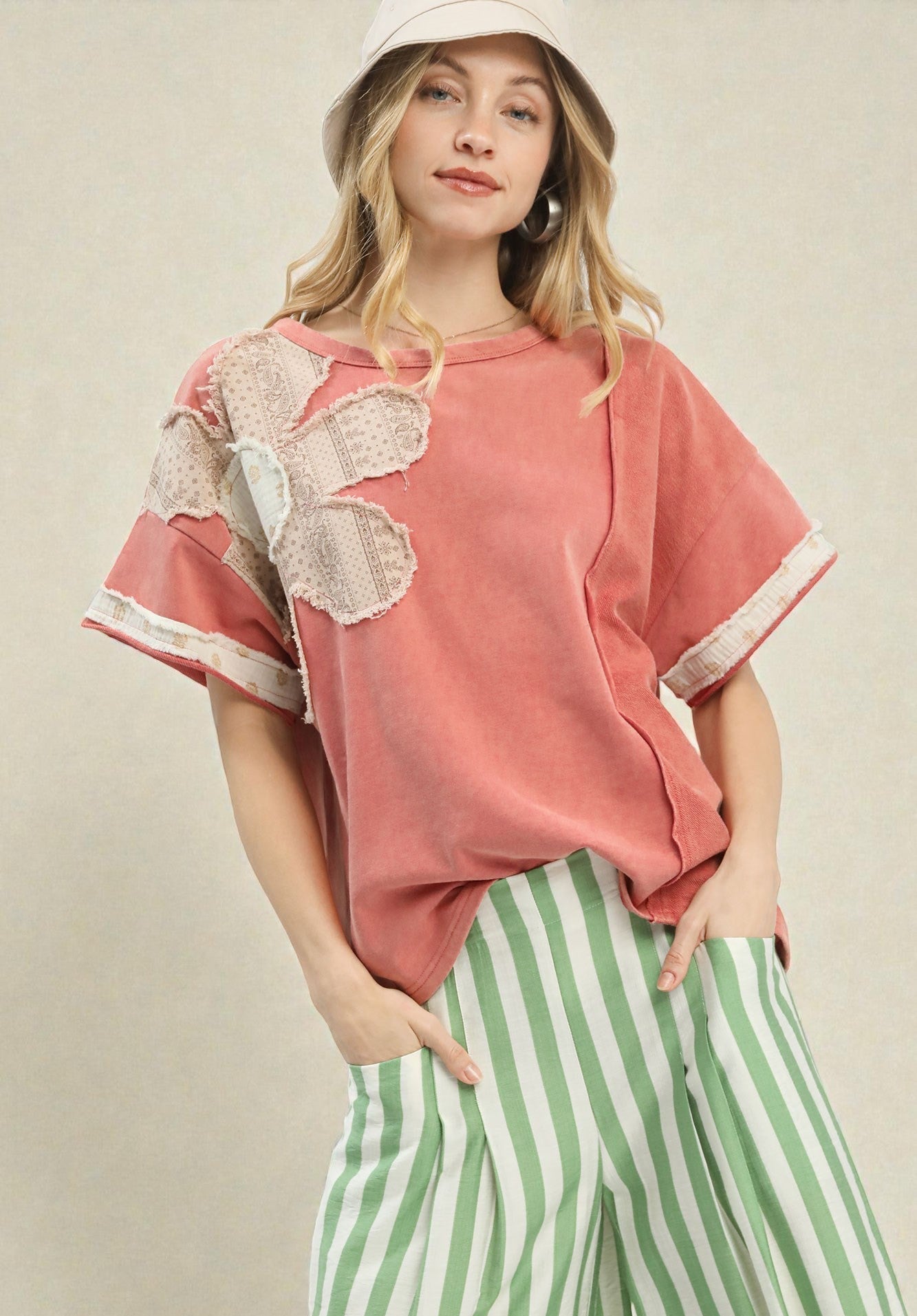 Woman wearing a pink top with lace sleeves and green striped pants on a beige background