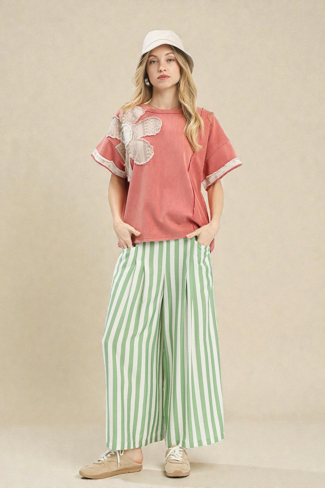 Woman wearing a pink top with floral details and green striped pants on a beige background