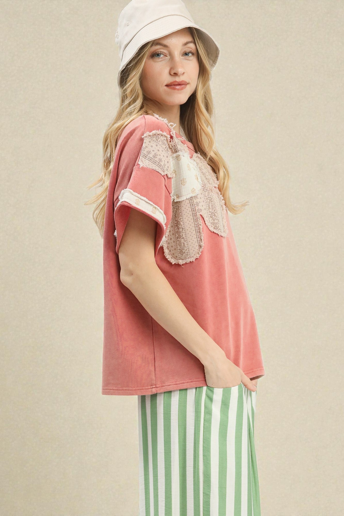 Woman wearing a pink top with lace details and green striped pants against a beige background