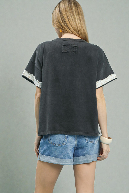 Person wearing a black t-shirt with white trim and denim shorts on a gray background