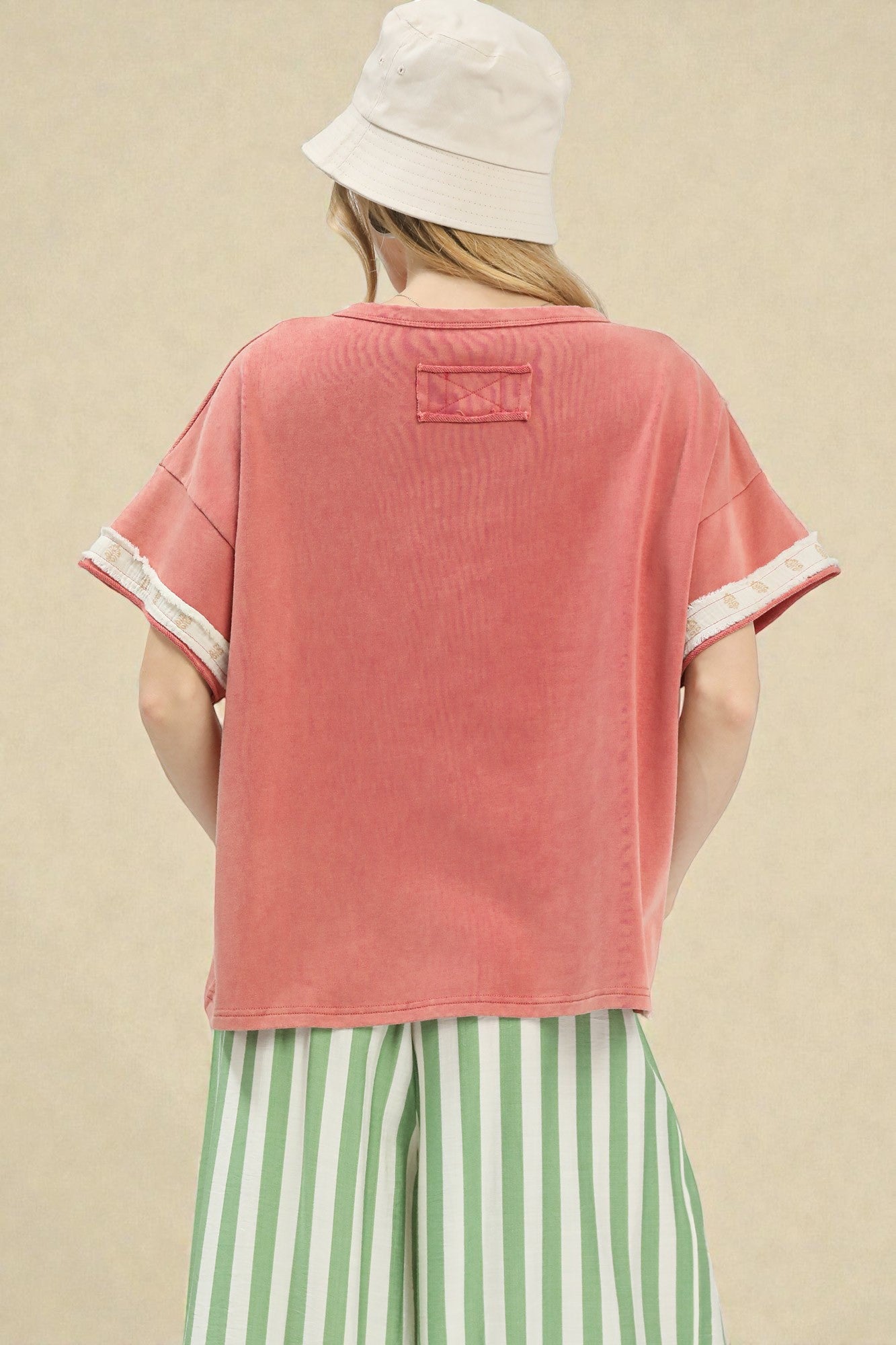 Person wearing a pink t-shirt with white trim and a white bucket hat on a beige background