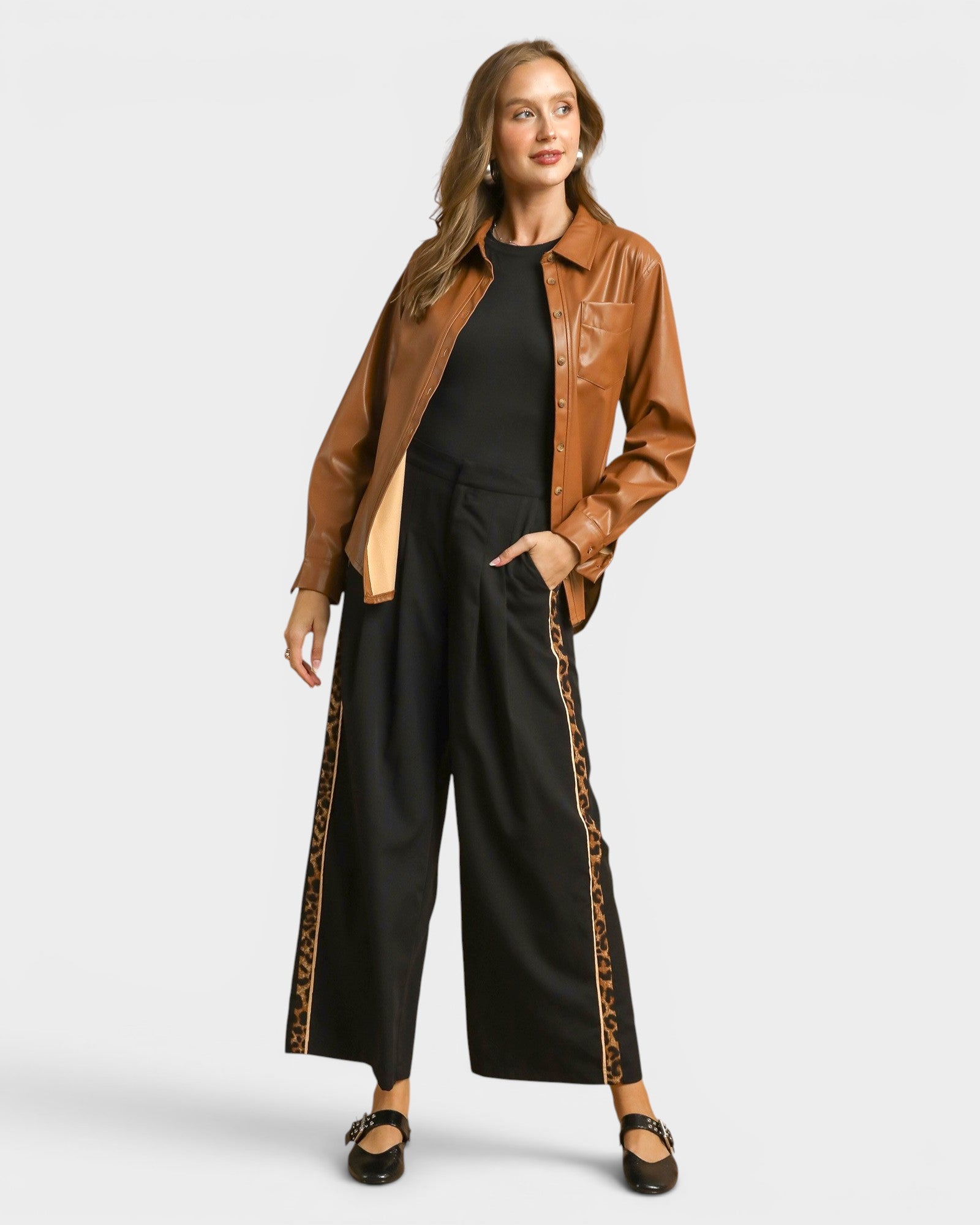 Woman wearing a brown leather jacket and black pants with leopard print trim on a white background