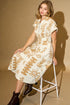 Woman wearing a patterned dress sitting on a stool against a beige background