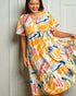 Woman wearing a colorful dress with abstract patterns against a white wall.