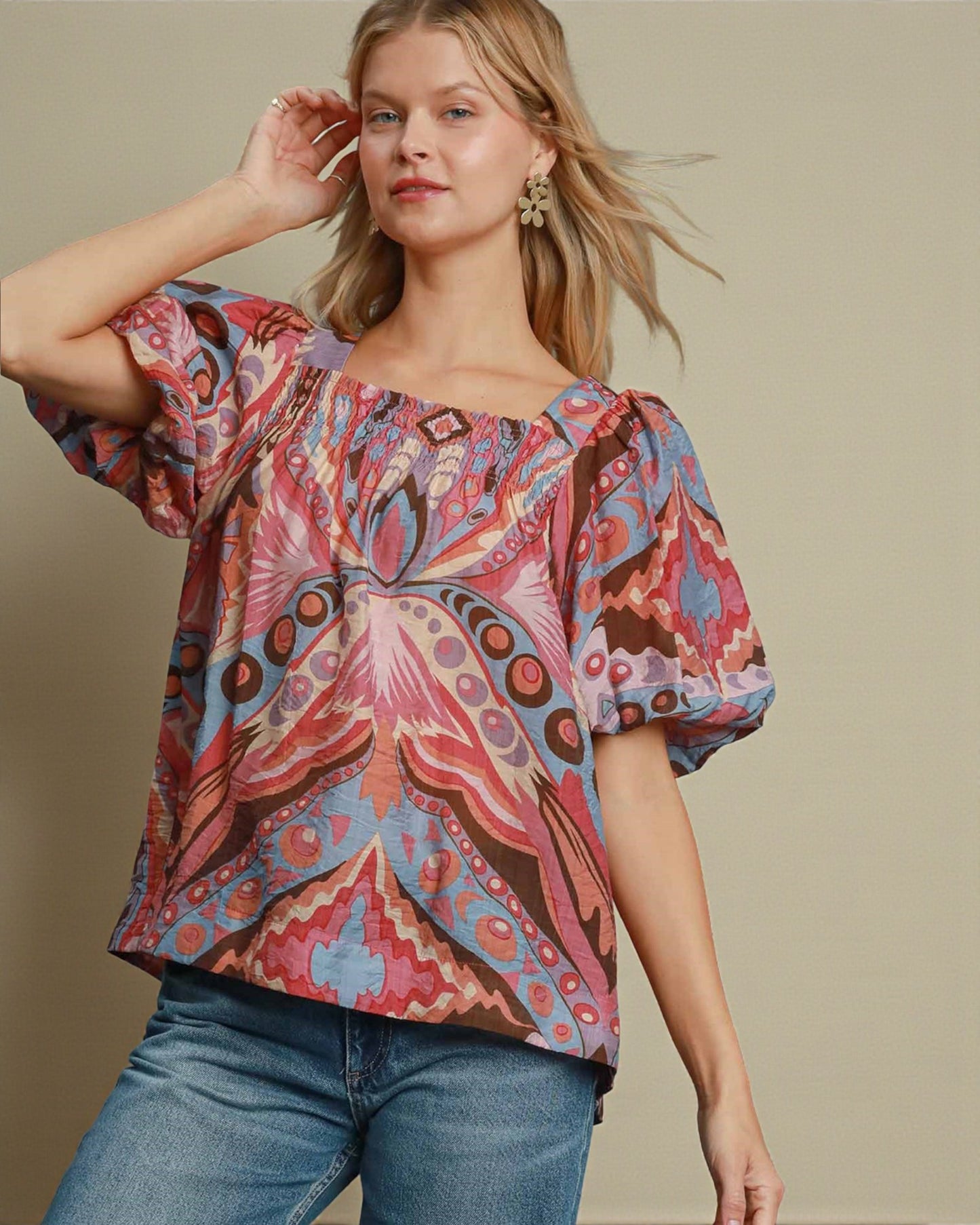 Woman wearing a colorful patterned blouse with blue jeans against a beige background