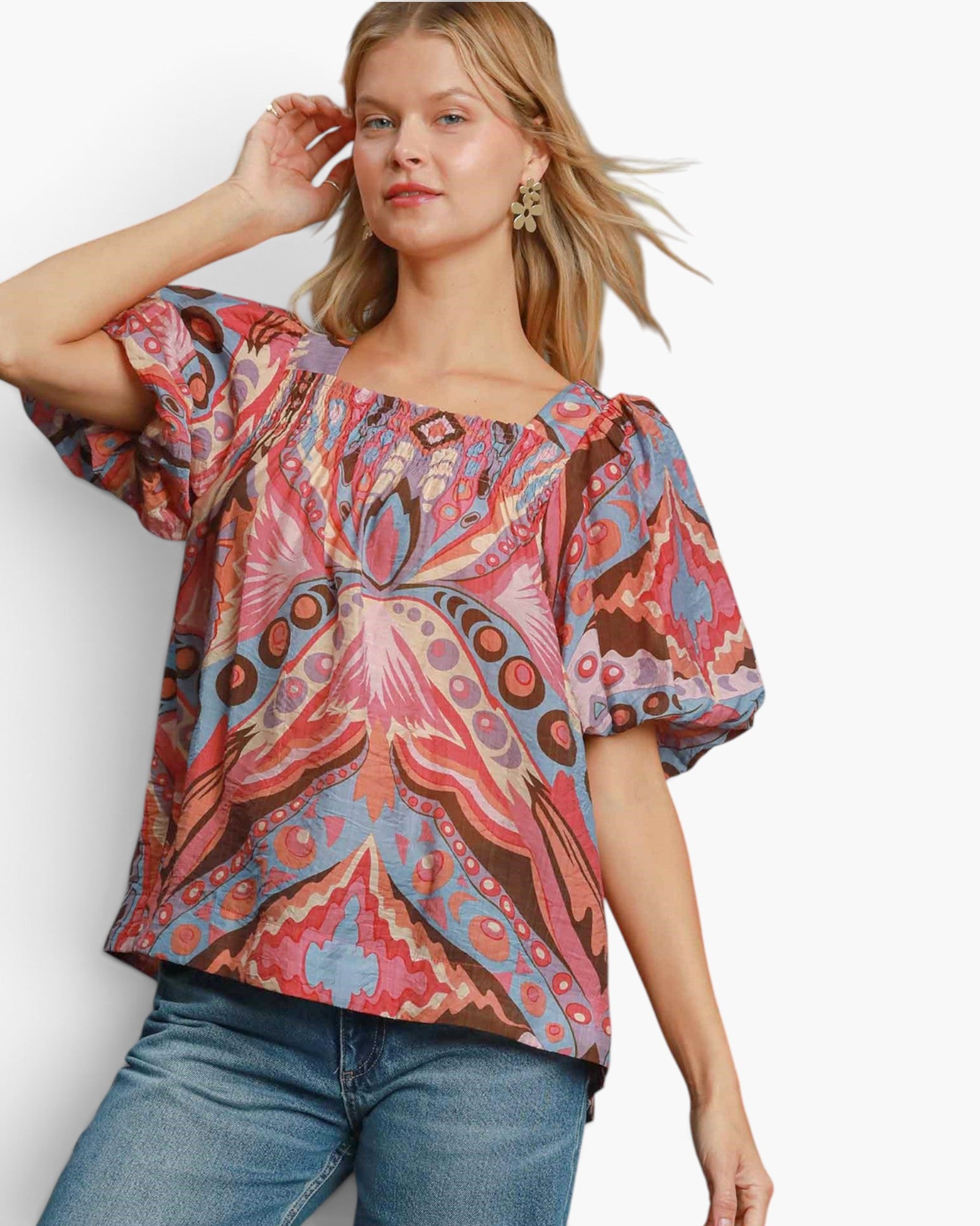 A woman wearing a colorful bohemian-style short-sleeve blouse with puff sleeves and an intricate paisley pattern, paired with blue jeans, against a plain white background.