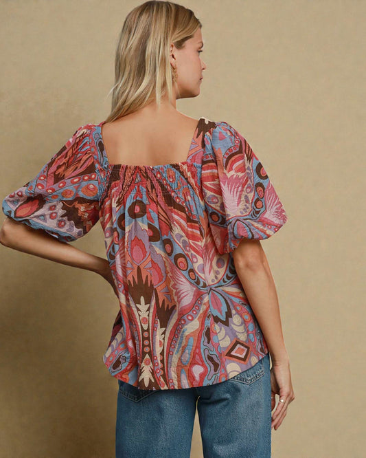 Woman wearing a colorful patterned blouse against a beige background