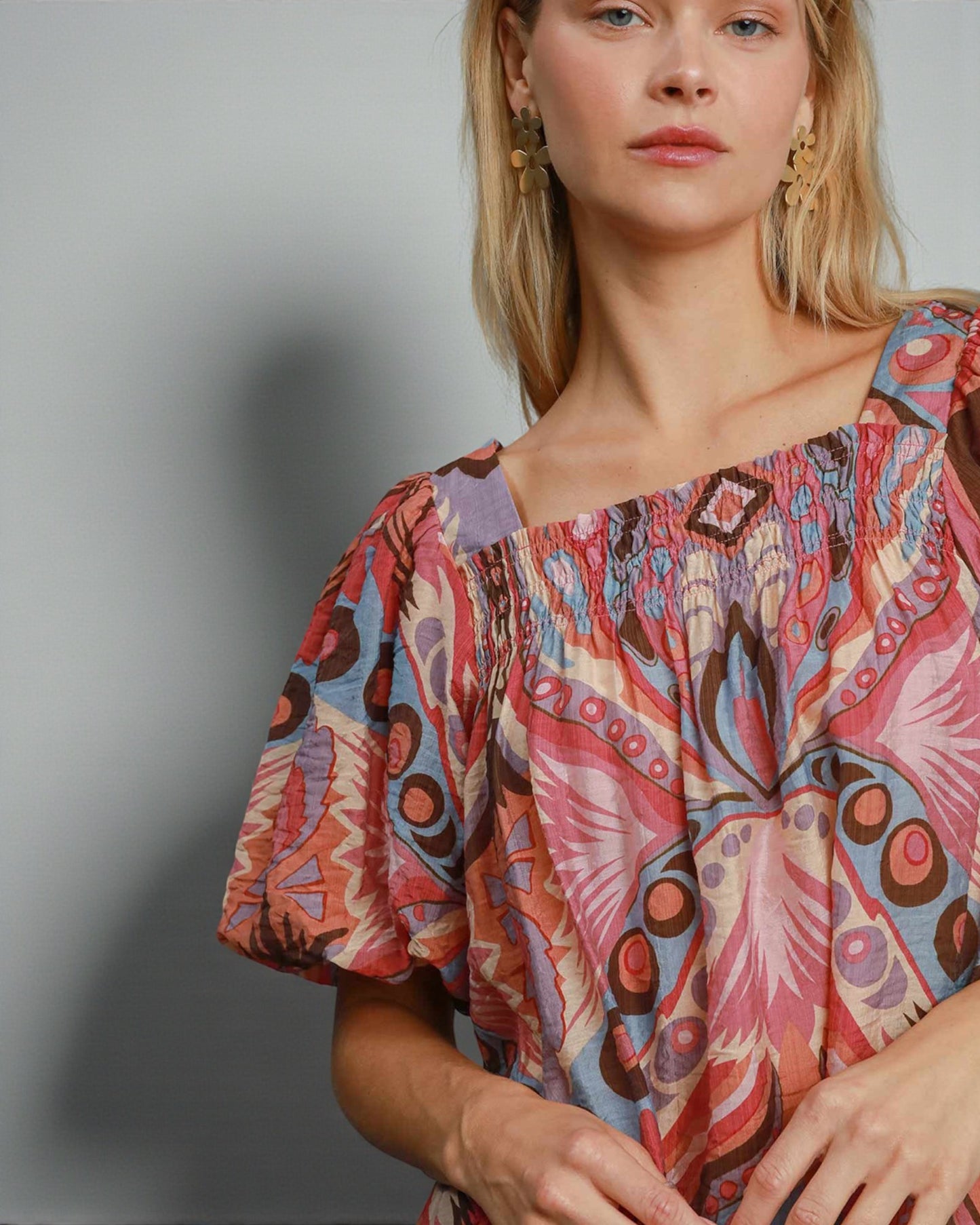 Woman wearing a colorful patterned blouse against a plain background