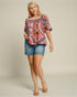 Woman wearing a colorful patterned top and denim shorts on a plain background